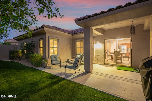 back house at dusk featuring a patio area and a lawn