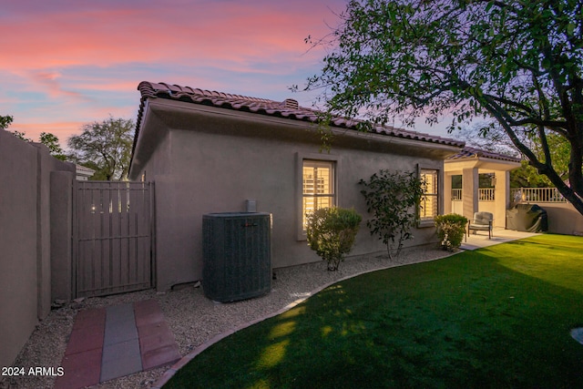 back house at dusk featuring central AC unit and a yard