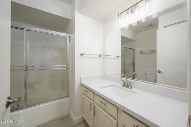 full bathroom featuring hardwood / wood-style flooring, vanity, combined bath / shower with glass door, and toilet