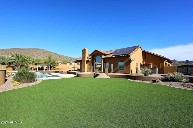 back of house featuring a lawn, a mountain view, solar panels, a fenced in pool, and a patio