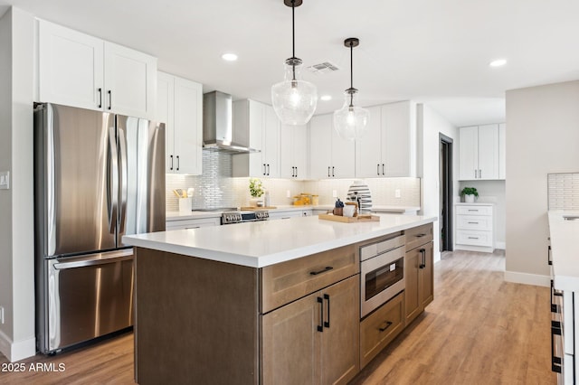 kitchen with stainless steel appliances, white cabinetry, and wall chimney exhaust hood