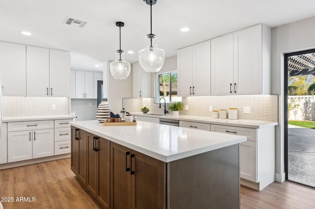 kitchen with light hardwood / wood-style floors, hanging light fixtures, a kitchen island, sink, and white cabinetry