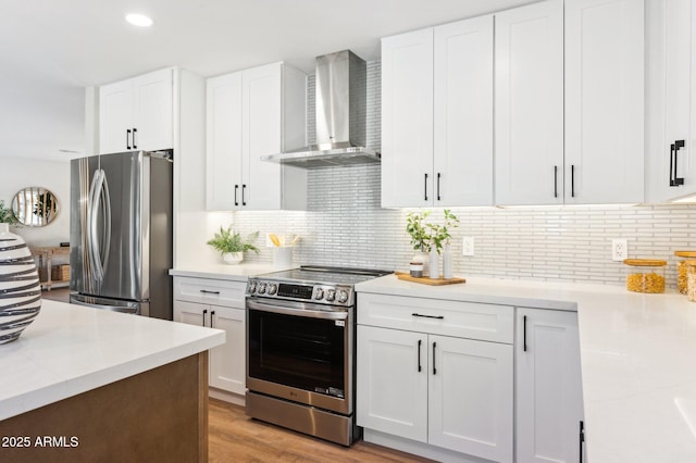 kitchen featuring stainless steel appliances, wall chimney range hood, tasteful backsplash, and white cabinetry