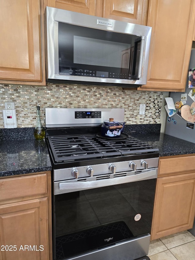 kitchen featuring light tile patterned floors, stainless steel appliances, light brown cabinetry, tasteful backsplash, and dark stone countertops