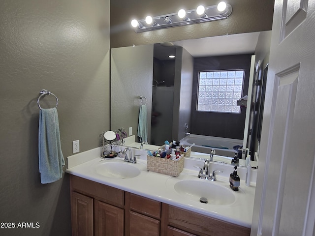 bathroom with a textured wall, double vanity, a sink, and a bath