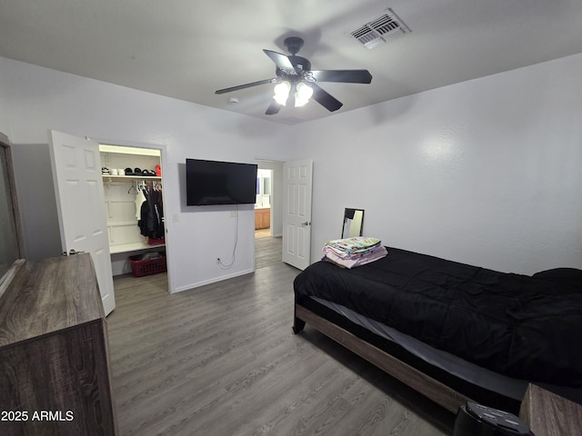 bedroom featuring a closet, visible vents, a spacious closet, a ceiling fan, and wood finished floors