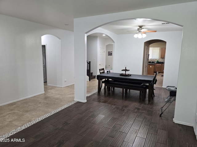 dining area with a ceiling fan, baseboards, arched walkways, and dark wood-type flooring