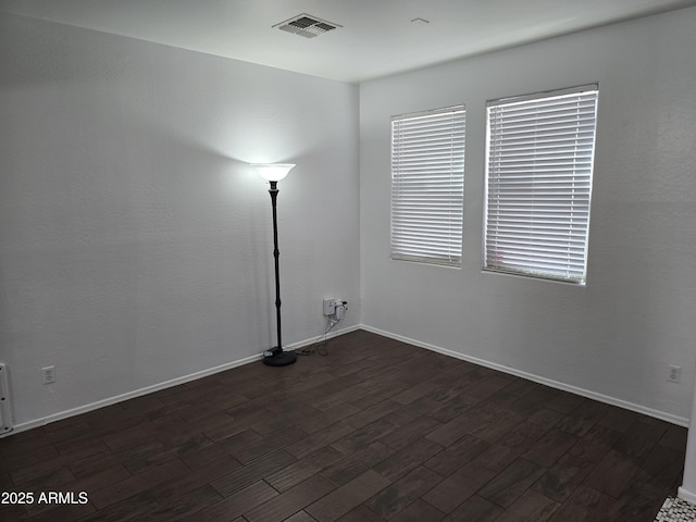 unfurnished room featuring dark wood finished floors, visible vents, and baseboards