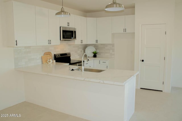 kitchen featuring light stone counters, stainless steel appliances, tasteful backsplash, a sink, and a peninsula