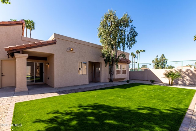 rear view of property with a yard, a patio area, fence, and stucco siding