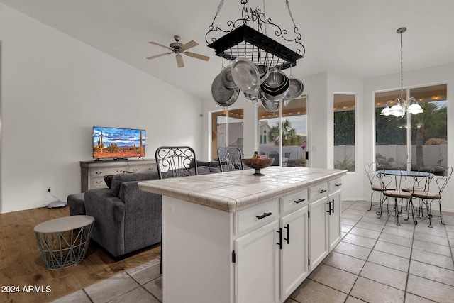 kitchen with white cabinetry, a center island, hanging light fixtures, tile countertops, and ceiling fan with notable chandelier