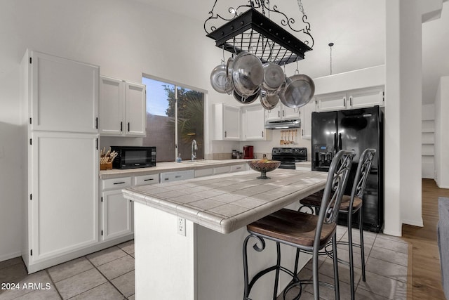 kitchen featuring a center island, tile counters, sink, white cabinets, and black appliances