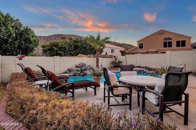 patio terrace at dusk featuring a fenced in pool