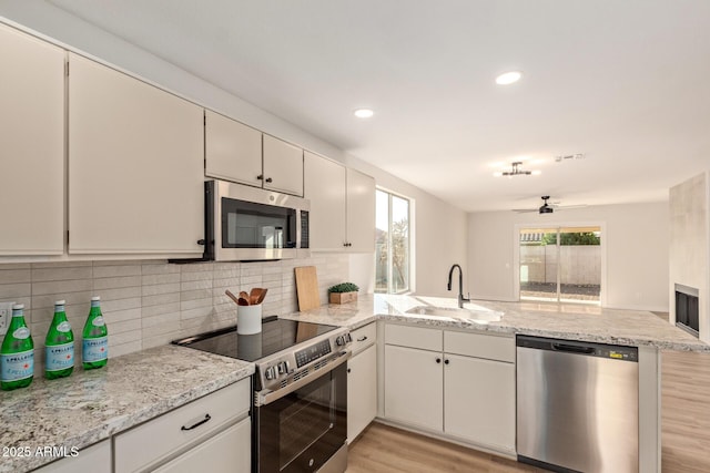 kitchen featuring ceiling fan, sink, stainless steel appliances, kitchen peninsula, and white cabinets