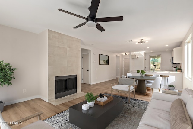 living room featuring a tile fireplace, hardwood / wood-style flooring, ceiling fan, and sink