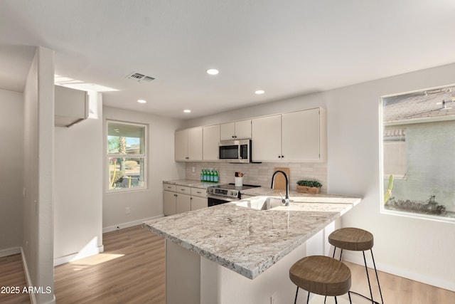 kitchen with white cabinets, light stone countertops, a kitchen bar, kitchen peninsula, and stainless steel appliances