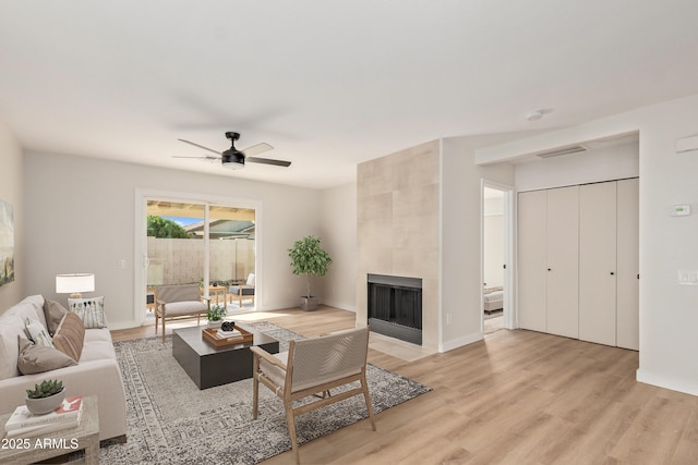 living room with ceiling fan, a tile fireplace, and light hardwood / wood-style flooring