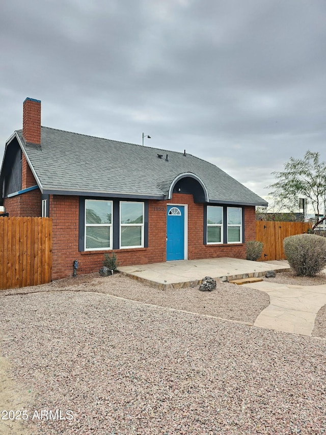 view of front of home featuring a patio, brick siding, a chimney, and fence