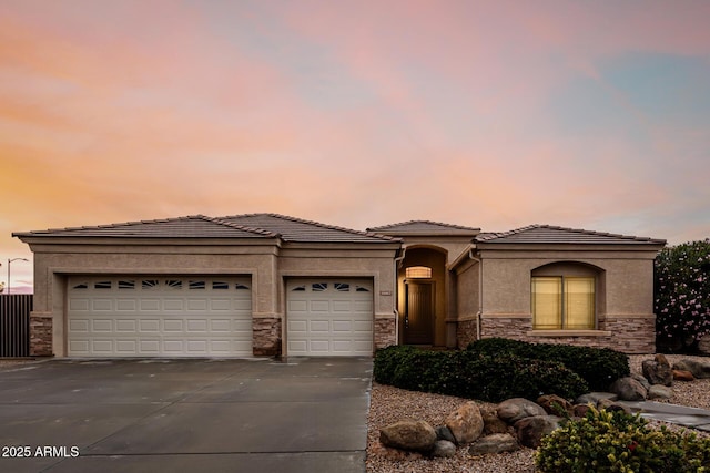 view of front of property with stucco siding, concrete driveway, a garage, stone siding, and a tiled roof