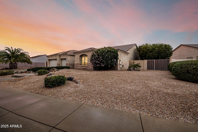 view of front of house with stucco siding, a gate, fence, a garage, and stone siding