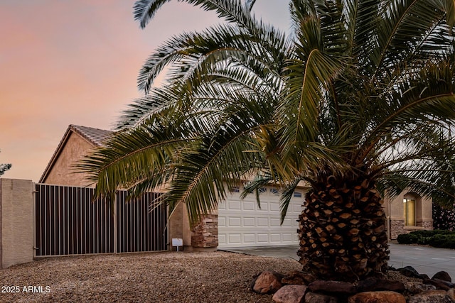 exterior space with a gate, driveway, an attached garage, and stucco siding