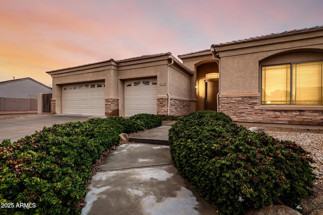 view of front of house with an attached garage, stone siding, concrete driveway, and stucco siding