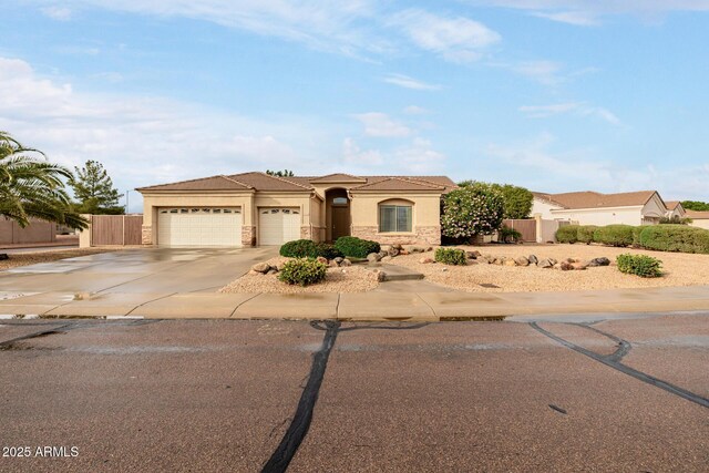 mediterranean / spanish home with stucco siding, concrete driveway, fence, a garage, and stone siding