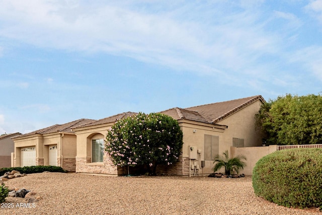 view of front of home with an attached garage, fence, stone siding, a tiled roof, and stucco siding