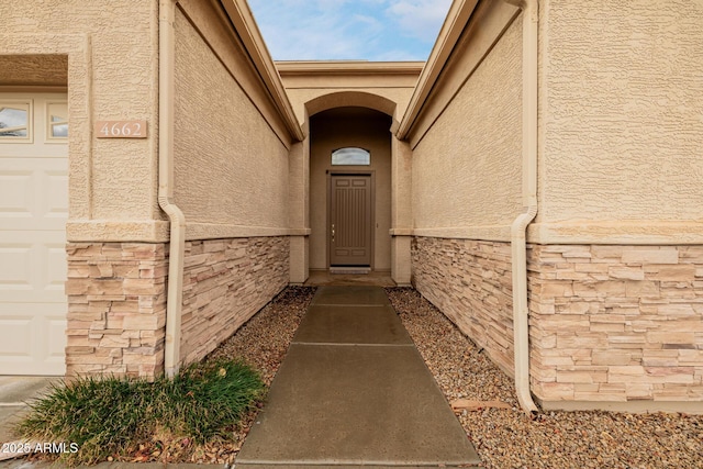 entrance to property with an attached garage, stone siding, and stucco siding