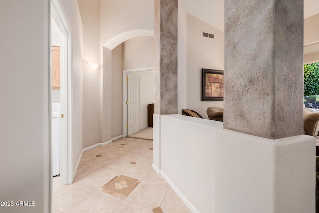 corridor with arched walkways, light tile patterned floors, a high ceiling, visible vents, and baseboards