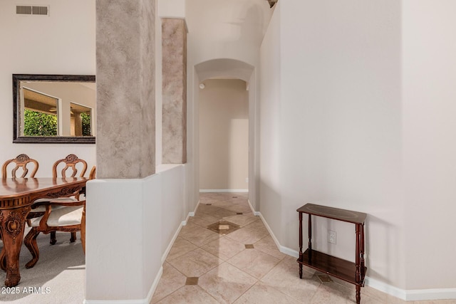 corridor with arched walkways, tile patterned flooring, visible vents, and baseboards