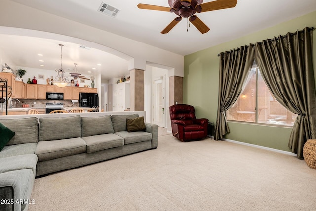 living room featuring baseboards, visible vents, arched walkways, light colored carpet, and ceiling fan