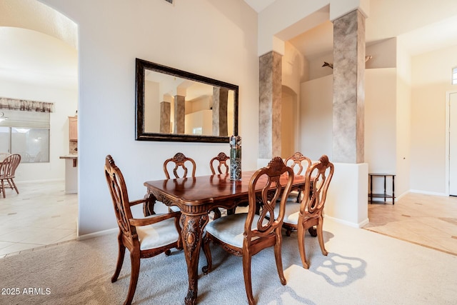 dining area featuring arched walkways, light tile patterned floors, ornate columns, light colored carpet, and baseboards