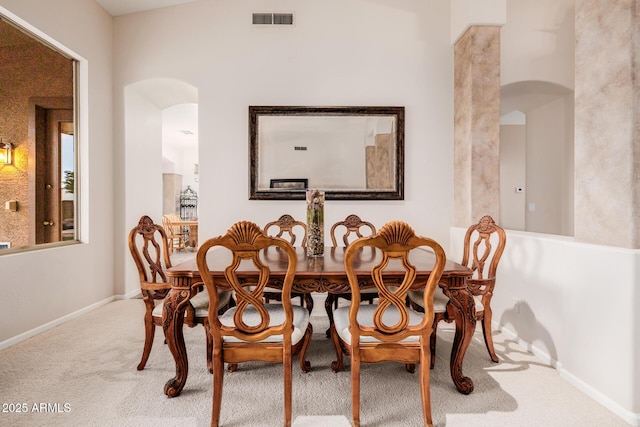 carpeted dining room with visible vents, arched walkways, and baseboards