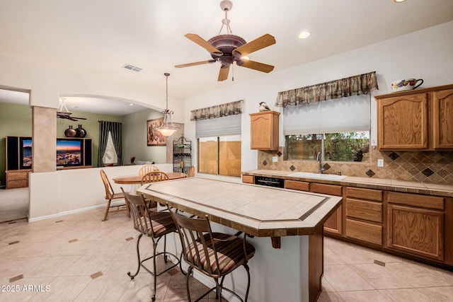 kitchen featuring a sink, visible vents, a kitchen breakfast bar, tile counters, and tasteful backsplash