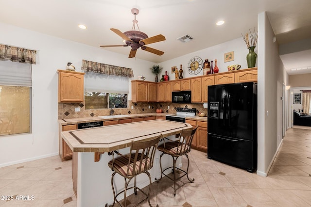 kitchen with a sink, a kitchen island, visible vents, black appliances, and tasteful backsplash