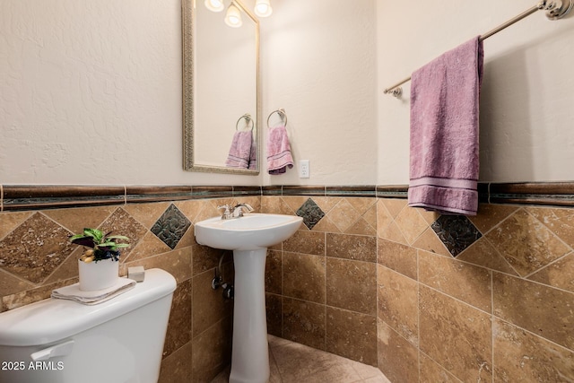 bathroom with toilet, tile walls, and wainscoting