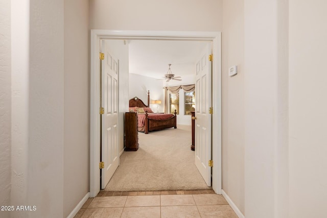 hall with light carpet, light tile patterned floors, and baseboards