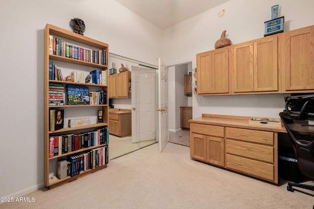 office space featuring light colored carpet, built in desk, and baseboards