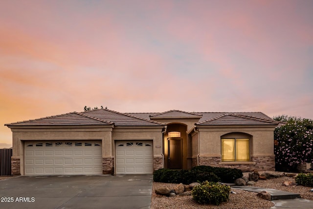 view of front of house with driveway, stone siding, a tile roof, an attached garage, and stucco siding