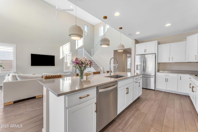 kitchen with sink, white cabinetry, appliances with stainless steel finishes, pendant lighting, and a kitchen island with sink