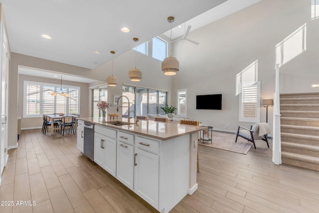 kitchen featuring decorative light fixtures, dishwasher, white cabinetry, sink, and a center island with sink