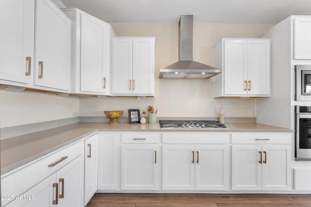 kitchen featuring stainless steel appliances, wall chimney range hood, white cabinets, and light hardwood / wood-style floors