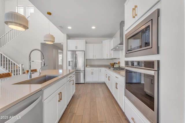 kitchen with appliances with stainless steel finishes, hanging light fixtures, wall chimney range hood, and white cabinets