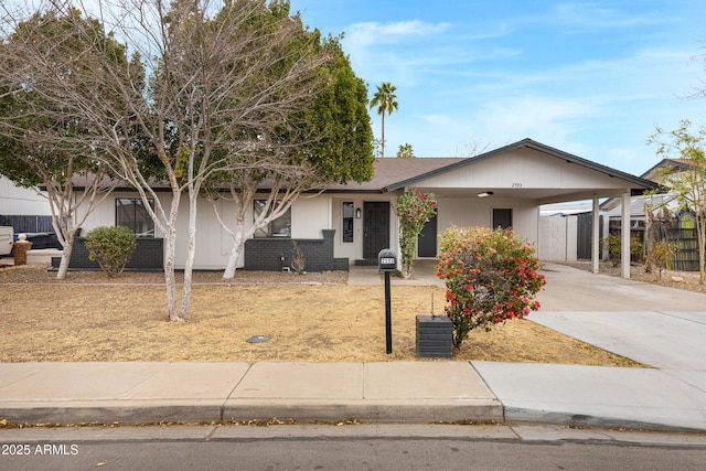 ranch-style home featuring concrete driveway, roof with shingles, fence, a carport, and brick siding