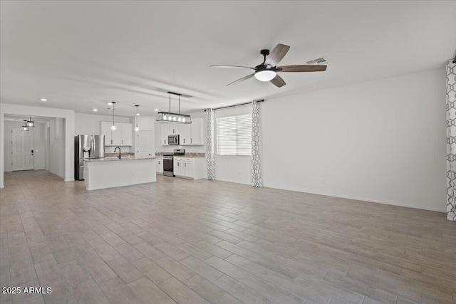 unfurnished living room featuring ceiling fan, sink, and light wood-type flooring