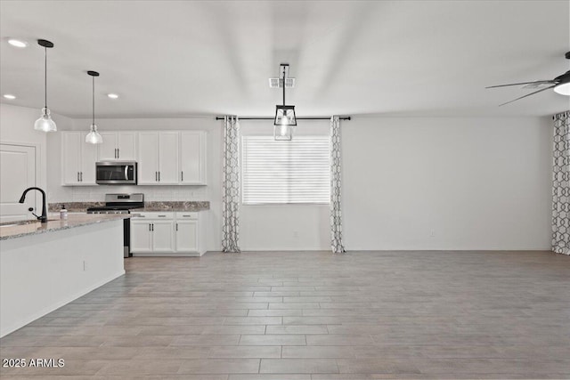 kitchen featuring decorative light fixtures, sink, white cabinets, stainless steel appliances, and light stone countertops