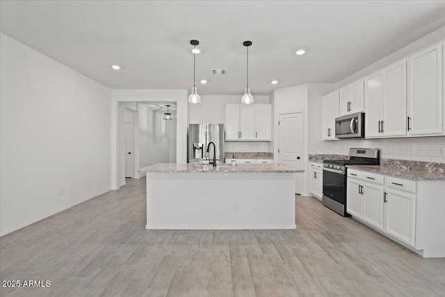 kitchen featuring light stone counters, appliances with stainless steel finishes, an island with sink, and white cabinets