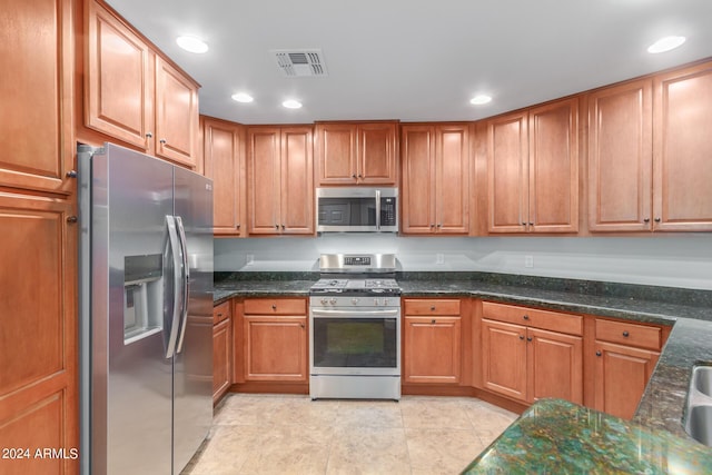 kitchen with light tile patterned floors, stainless steel appliances, and dark stone counters