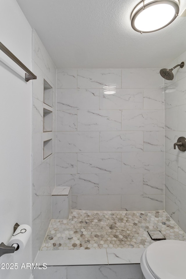 bathroom with a tile shower, a textured ceiling, and toilet